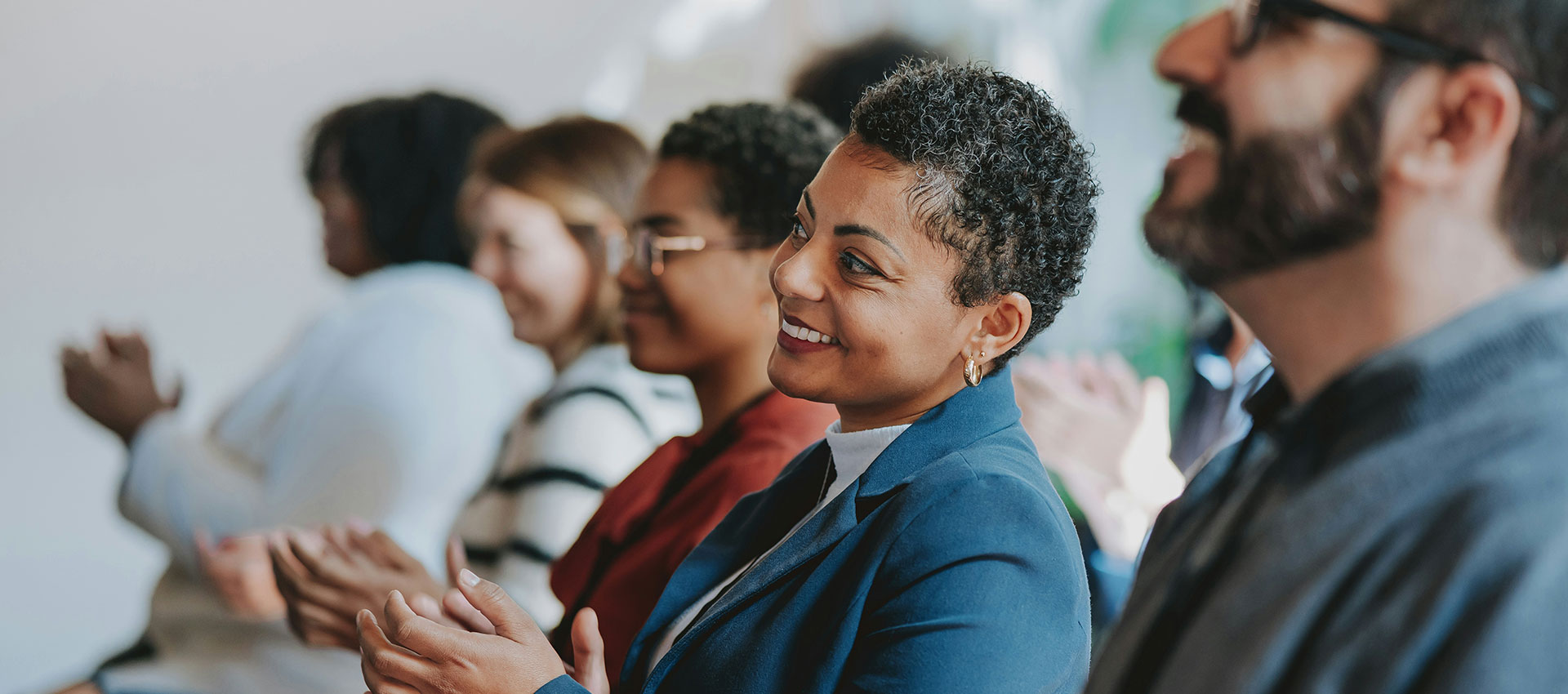 A man and three woman sat on the front row clapping a the speaker at a professional event.