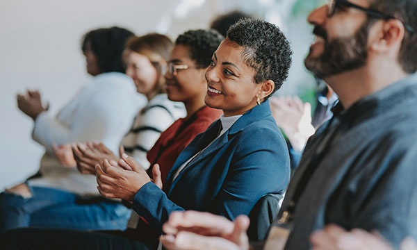 A man and three woman sat on the front row clapping a the speaker at a professional event.