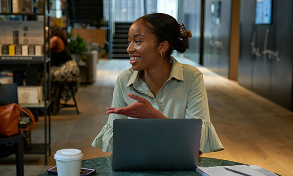 A young black woman sat at her desk in a modern office talking to someone off camera.