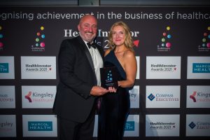 A woman in a formal black dress receives an award from a man in a black tuxedo.