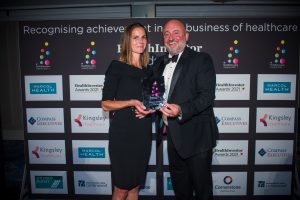 A woman in a formal black dress receives an award from a man in a black tuxedo.
