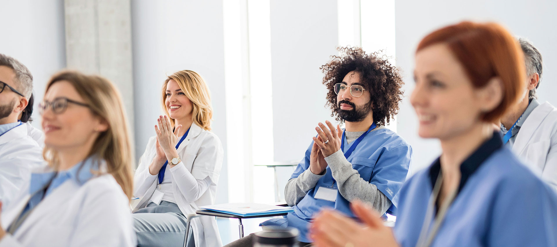 Medical staff clapping while sat in the audience of a conference talk.