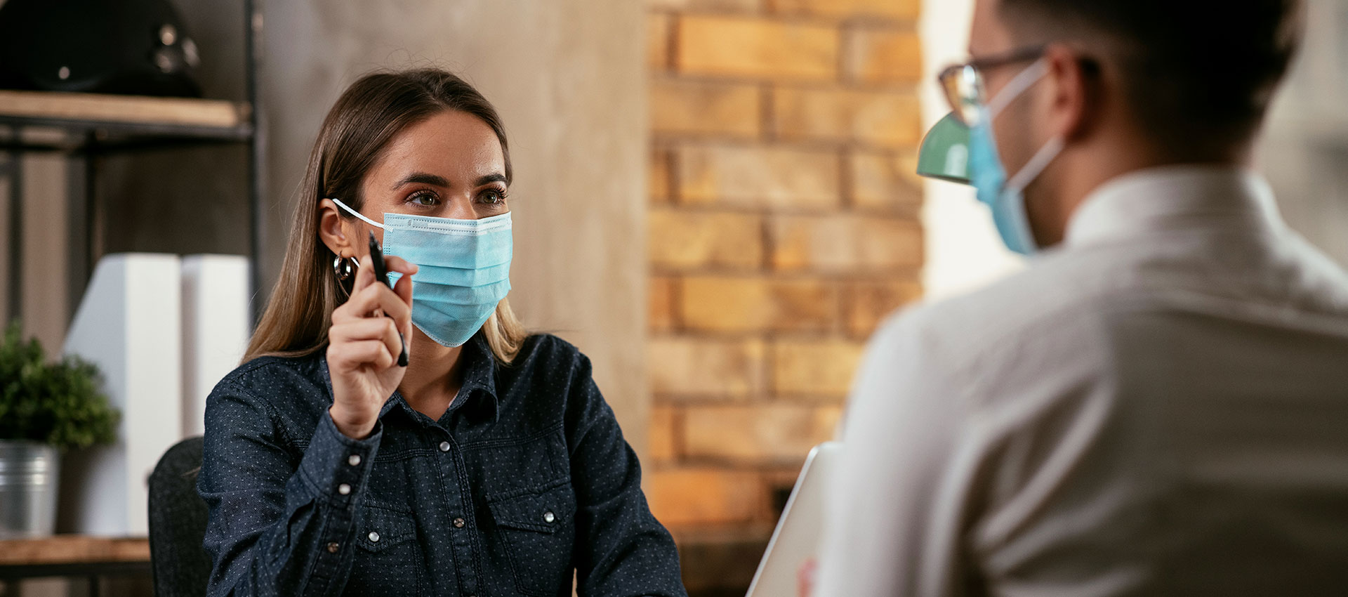 Man and woman sat in a meeting with surgical masks over their mouths.