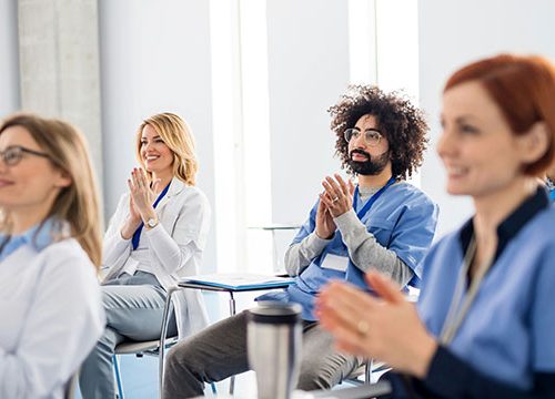 Medical staff clapping while sat in the audience of a conference talk.