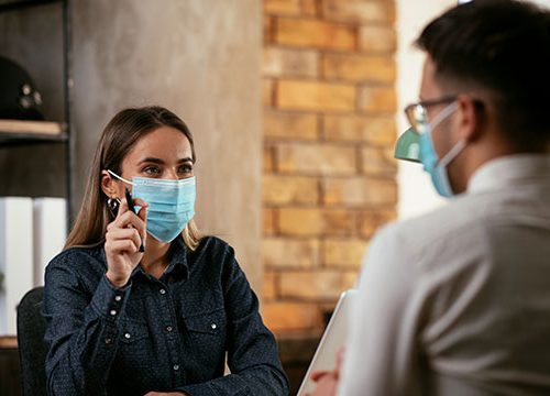Man and woman sat in a meeting with surgical masks over their mouths.