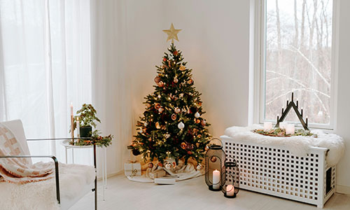 A small Christmas tree with pink baubles, lights and gold star sits in the corner of a white painted living room.