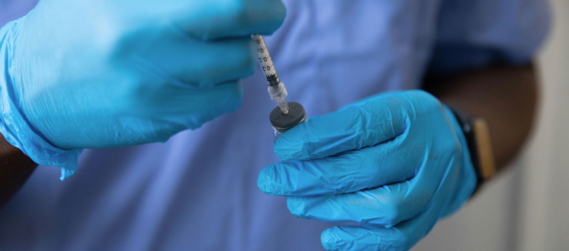 Close up of a black male nurse wearing surgical gloves and holding a syringe.