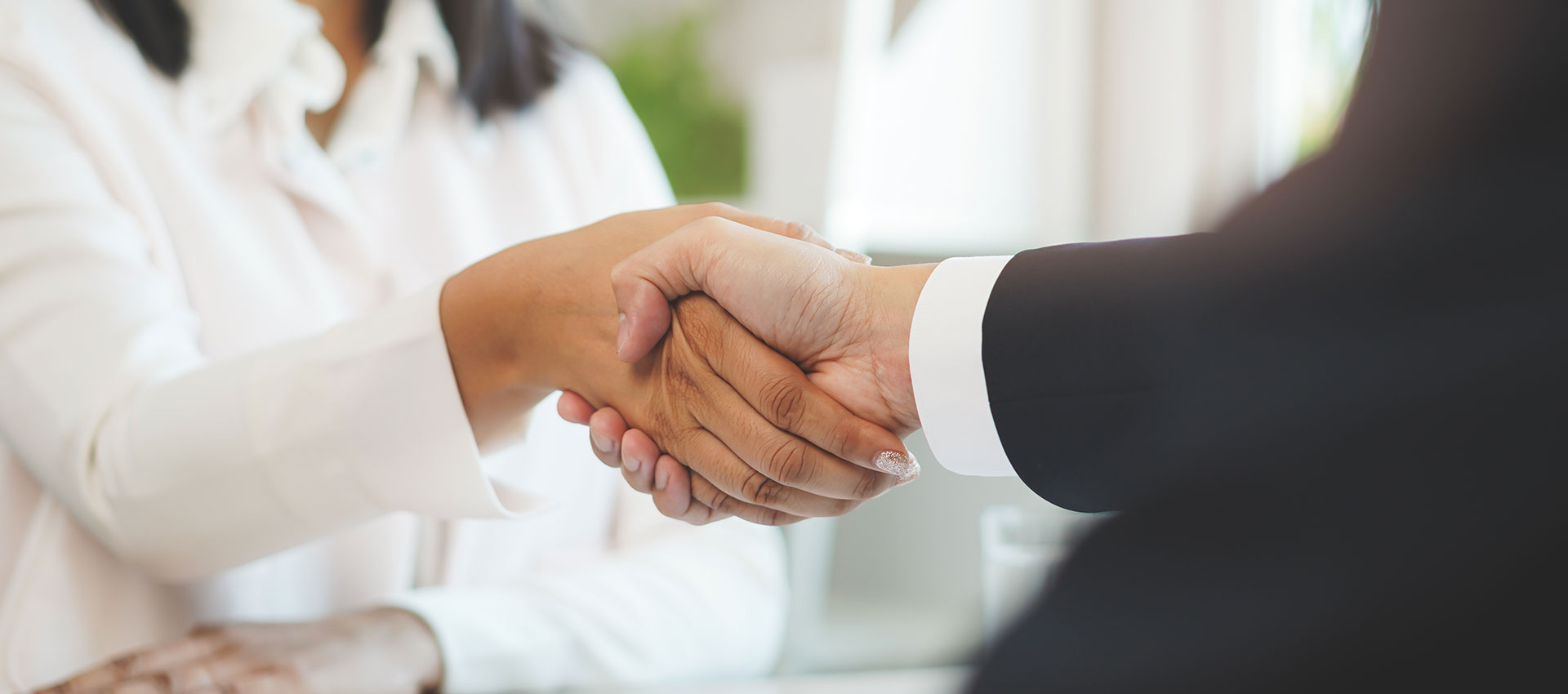 Close up of a man in a suit and a woman in a white shirt shaking hands.