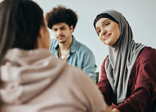 A woman wearing a hijab sits next to a man while talking to a girl in a pink hoody.