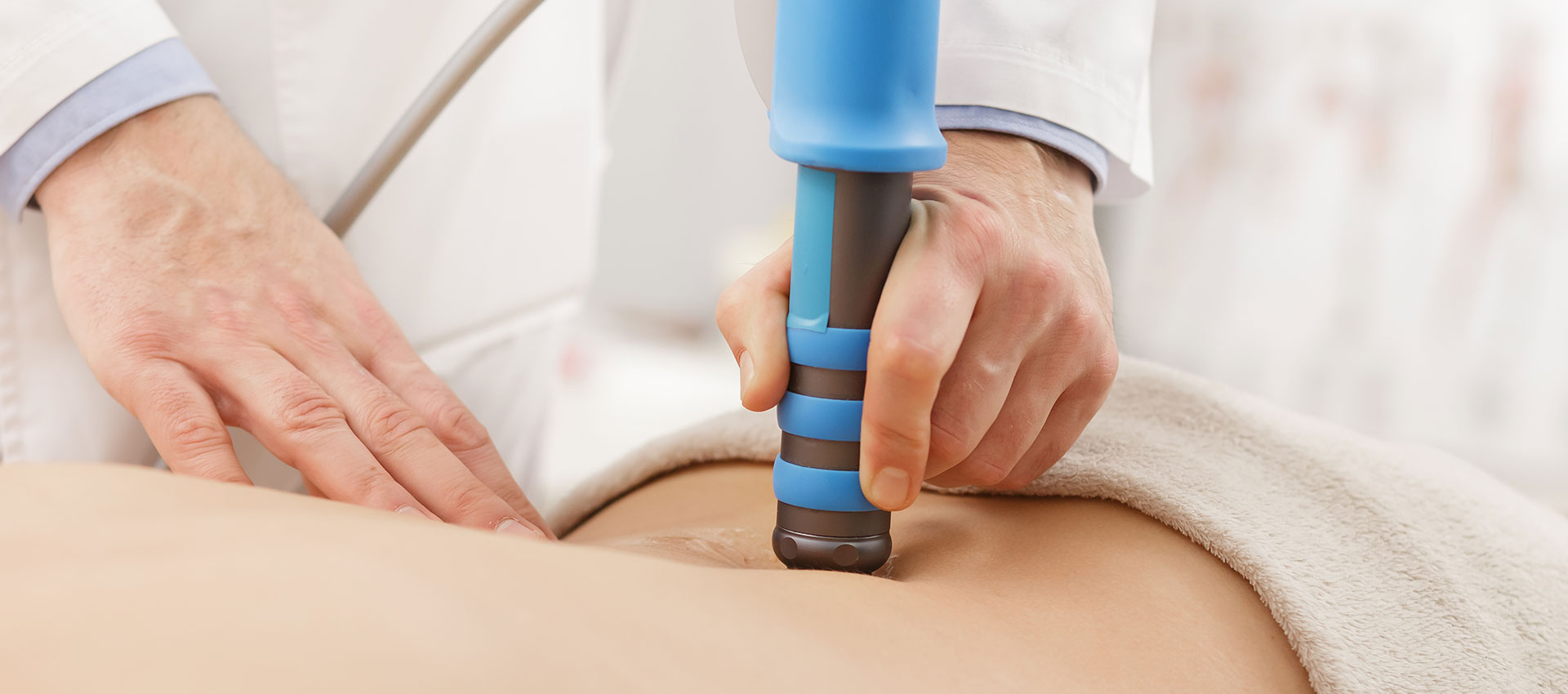 Close up of a medical professional using a blue and grey shockwave therapy machine on a patients the lower back.