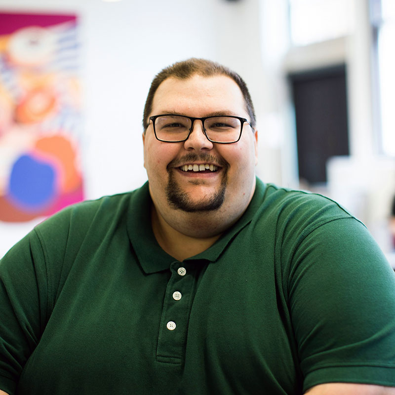 A man wearing a green polo top and glasses with goatee facial hair smiles at the camera.