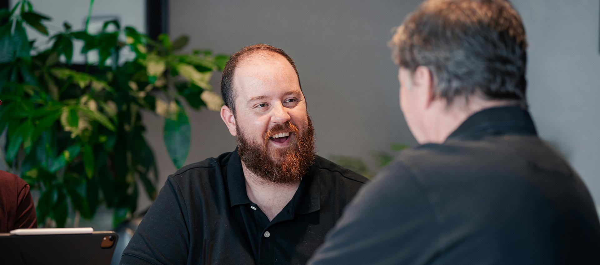 Two men in black polo tops sat in an office talking.