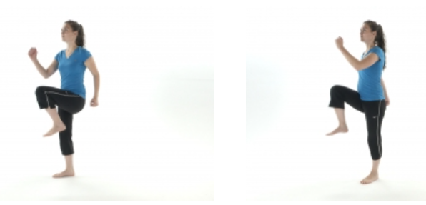 A woman in a blue shirt and black pants performs high knee exercises, alternating legs, against a plain white background. Her posture is upright and balanced.