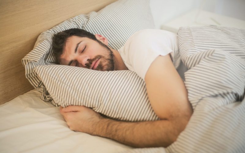 A man sleeps on a bed, hugging a striped pillow in a cozy bedroom with matching striped bedding.