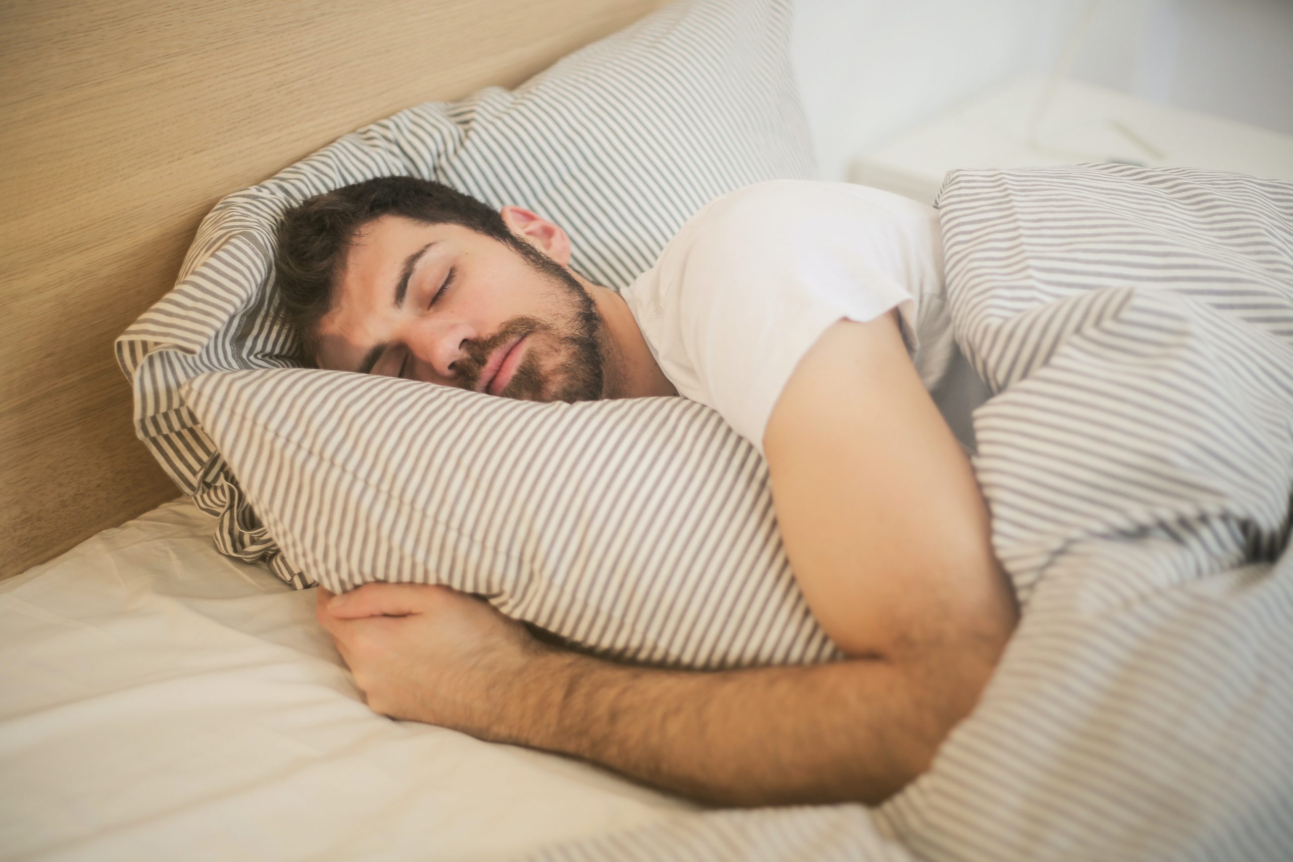 A man sleeps on a bed, hugging a striped pillow in a cozy bedroom with matching striped bedding.