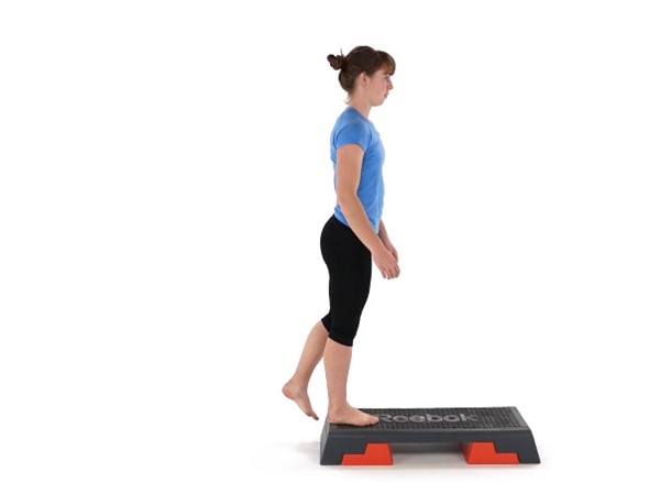 A person steps backward off a Reebok-branded exercise step, maintaining balance, against a plain white background.