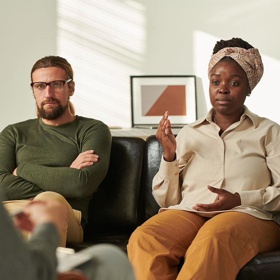 Three people are seated in a room with light-colored walls. One person is speaking while the others listen attentively, suggesting a counseling or discussion session. No text present.