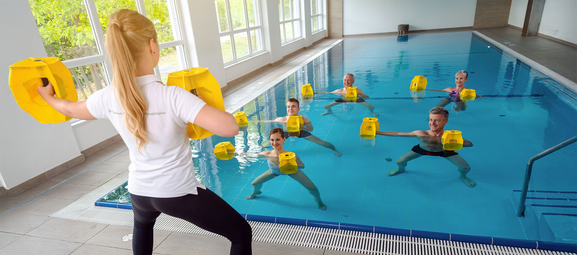 Instructor leads a water exercise class in a bright indoor pool. Participants hold yellow floatation devices and mirror her movements, surrounded by large windows and tiled floors.