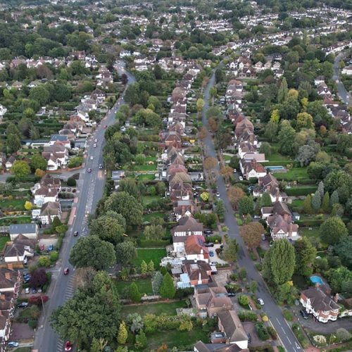 Aerial view of a residential neighborhood with rows of houses lined with trees on both sides of the streets, surrounded by lush greenery, extending into the distance.