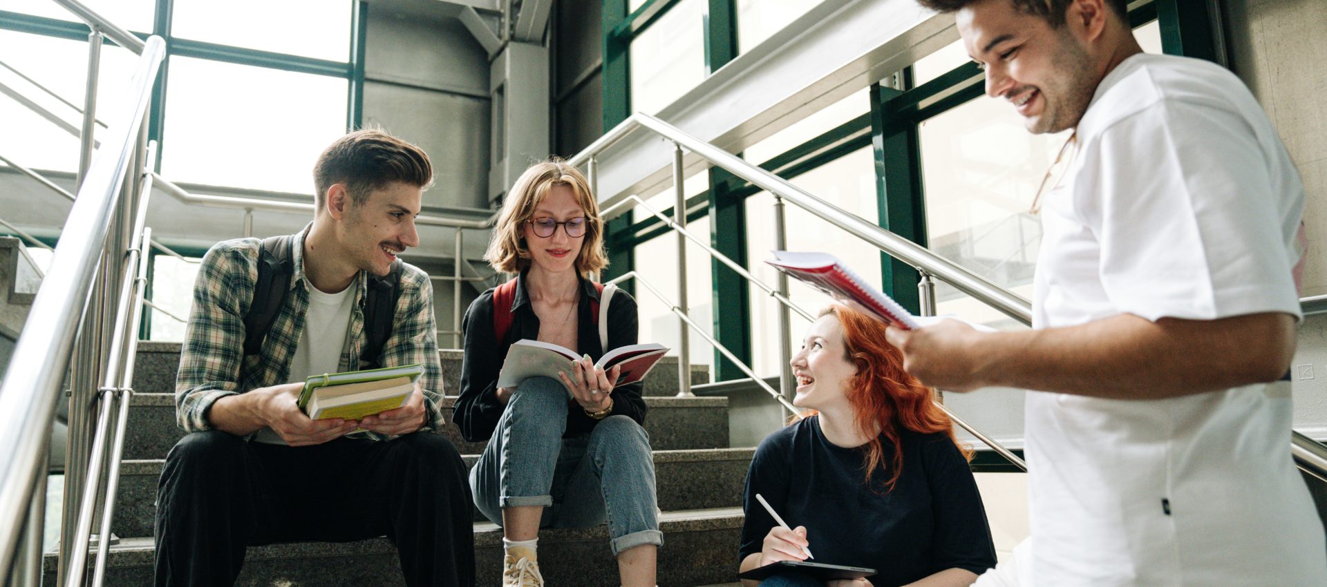 A group of student sit on a stairwell inside a university, talking and comparing notes.