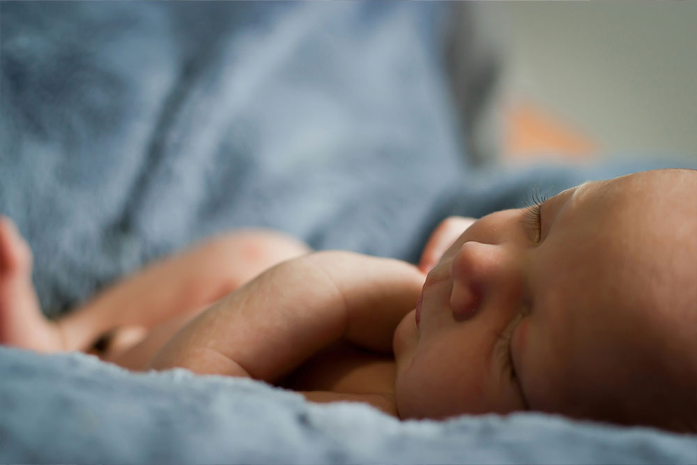 Newborn baby sleeping peacefully, nestled in a soft, blue blanket, creating a calm and cozy atmosphere.