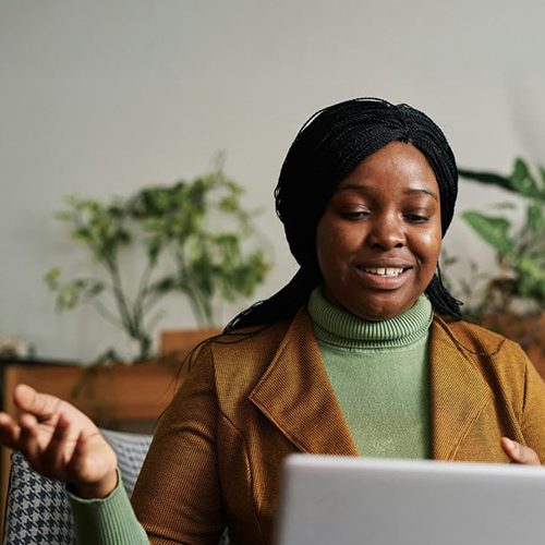 A woman talking to a laptop whilst sitting on a chair in a cozy room.
