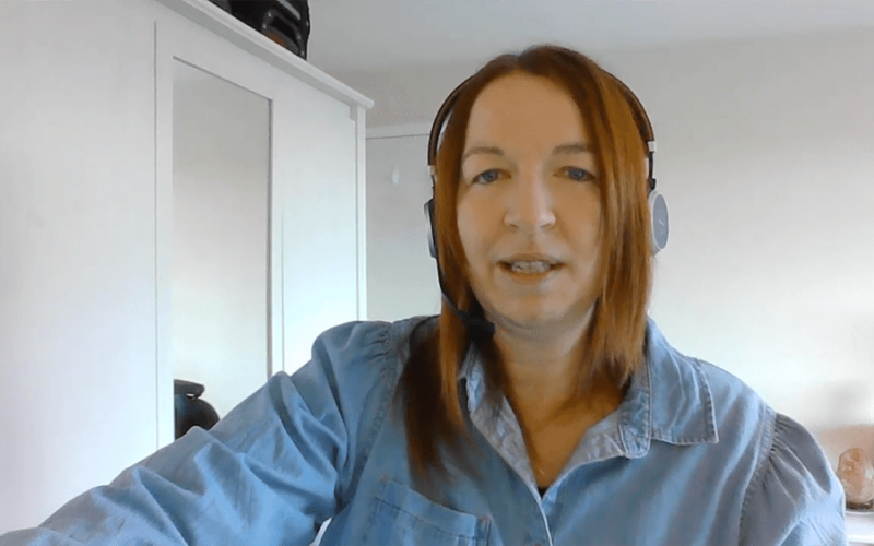 A screen capture of webinar where a woman with ginger hair speaking while wearing a headset, seated in a room with a white wardrobe and mirrored cabinet in the background.