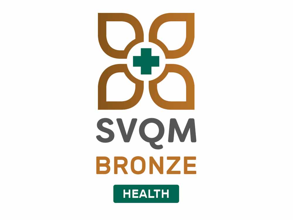 Logo with a green plus symbol reflecting healthcare surrounded by four gold leaves creating a flower symbol. Underneath the text SVQM sits in silver with the text 'BRONZE' underneath in gold.